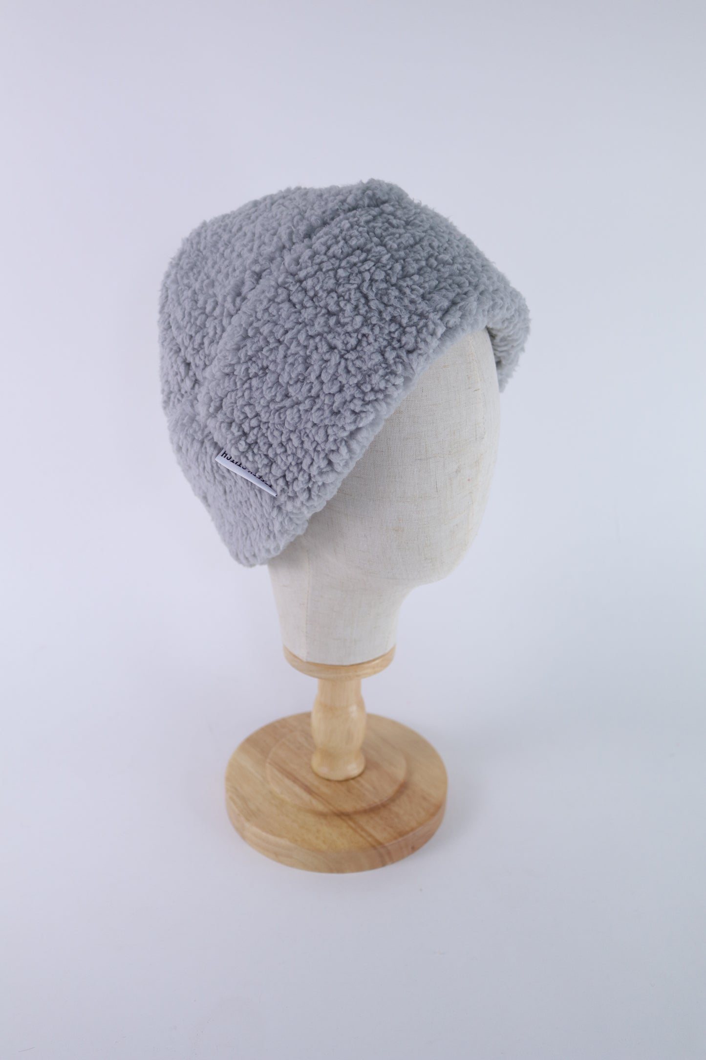 Gray faux sherpa beanie displayed on a cream mannequin head with a wooden stand, shown in side view.