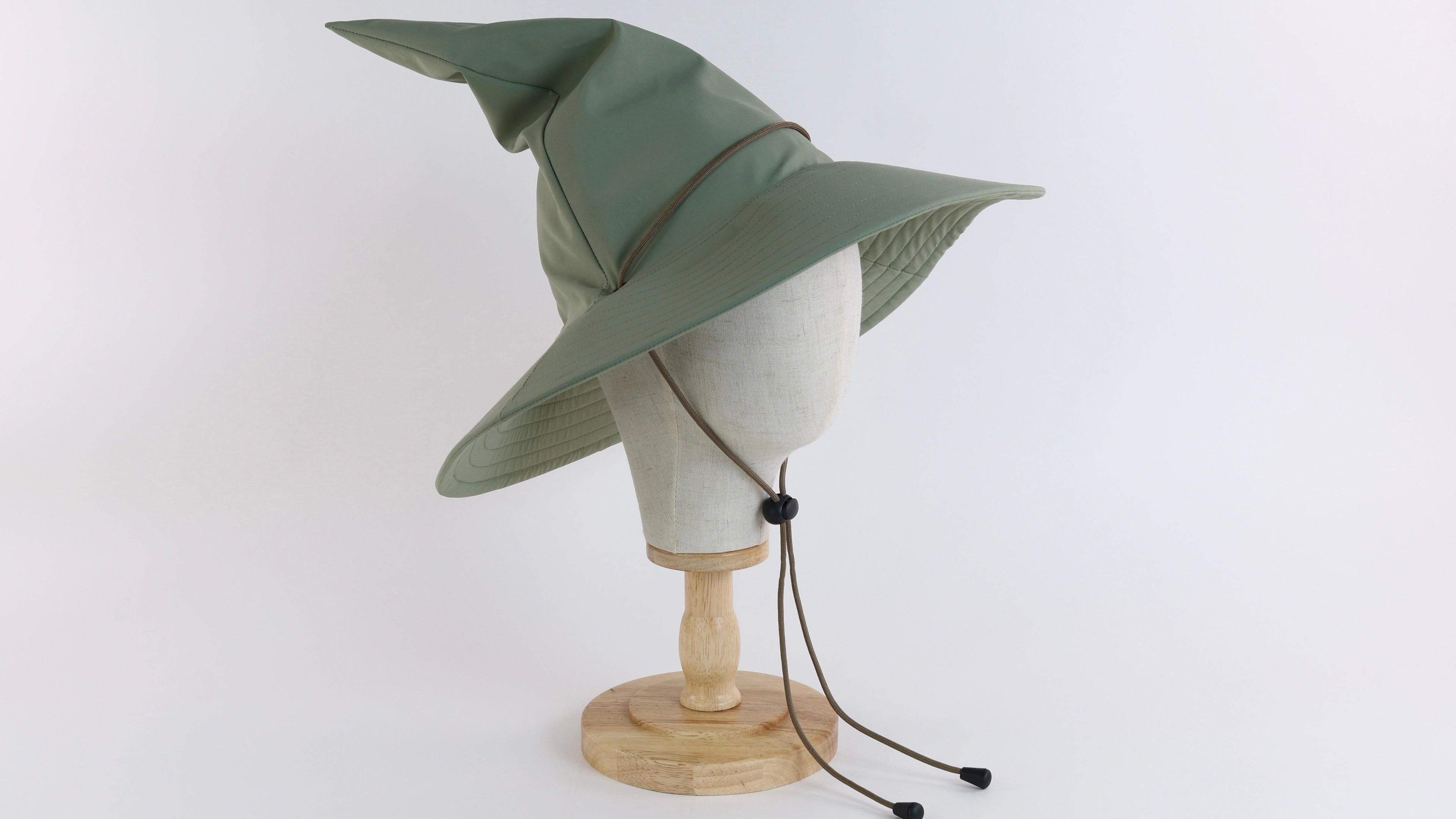 sage green wizard hat with brown chin strap on a cotton head mannequin against a white background